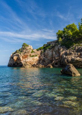 İspanya, Mallorca, Deia köyü yakınlarındaki resim gibi bir sahil şeridi. Akdeniz 'in turkuvaz sularına kayalıklar iniyor.