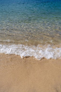 Gök mavisi deniz dalgaları yavaşça kumlu kumsala yuvarlanarak makarna oluşturur. Kumsalda güneşli bir gün. Yaz tatili kavramı.