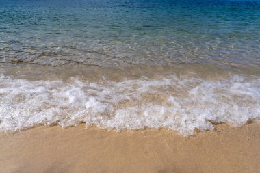 Gök mavisi deniz dalgaları yavaşça kumlu kumsala yuvarlanarak makarna oluşturur. Kumsalda güneşli bir gün. Yaz tatili kavramı.