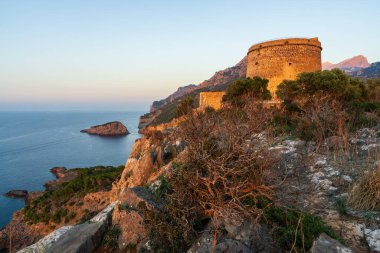 Eski gözetleme kulesi Torre Picado güneş batarken kayalık Port de Soller üzerinde kuleler. Ilık altın rengi taş duvarlar.