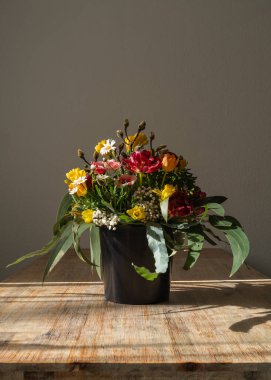 Masanın üzerinde büyük renkli buket taze çiçekler duruyor. Atmosfer neşe, tazelik ve kutlama yaratır.