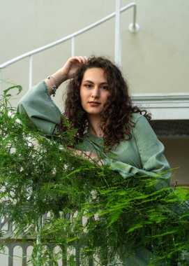 Beyaz merdivenlerde duran güzel genç kadın yemyeşil bitkilerle çevrili, zarafet ve sükunetle doğal atmosfer yaratıyor..