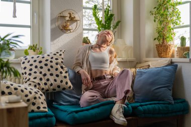 Oturma odasında, mutlu sarışın kadın kanepeye yaslanıyor. Avrupalı kadınlar hafta sonu ya da tatilin tadını çıkarıyor.