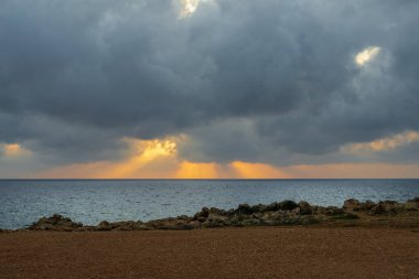 Kıbrıs Rum Kesimi 'nin Peyia kentindeki kayalık kıyı şeridinde gün batımı. Çarpıcı doğal zıtlıklar ve sakin atmosfer burayı seyahat, doğa ve rahatlama için ideal kılıyor..