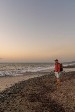 Sahildeki yürüyüşçü silueti gün batımında suyun üzerinde. Huzurlu bir düşünce ve keşif anı..