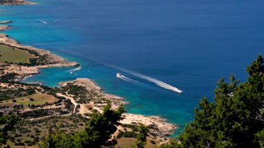 Kıbrıs 'ın Fontana Amorosa kenti yakınlarındaki yabani sahil ve kristal berraklığında Mavi Göl manzaralı insansız hava aracı. Suyun üzerindeki sürat tekneleri bu sevgili adanın atmosferini canlandırıyor.. 