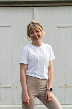 Beyaz ahşap kapının arka planında poz veren hafif gündelik kıyafetli neşeli genç kadın portresi. Yaşam tarzı, moda, gençlik ve basitlik kavramı.