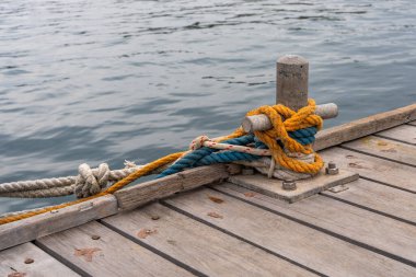 Tahta iskeleye yerleştirilmiş, etrafını saran renkli, canlı iplerle demirleme bölmesine yakın durun. Arka planda sakin deniz görünüyor. Denizcilik ayrıntıları deniz seyahatini, tekneyi simgeliyor.