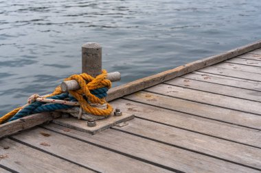 Denizin kıyısındaki ahşap güvertedeki metal yığının etrafındaki renkli rıhtım çizgileri. Yakından denizcilik müfrezesi kıyı seyahatinin ve yelkenciliğin özünü yakalıyor.