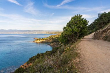 Kıbrıs 'ta Akdeniz boyunca manzaralı yürüyüş yolu. Açık hava, açık mavi deniz, kayalık arazi. Turistler arasında yürüyüş ve yürüyüş güzergahı.