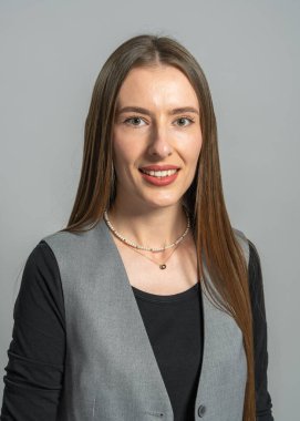 Profesyonel makyajlı gülümseyen genç bir kadın tarafsız bir arkaplanda poz veriyor. Doğal güzelliği yansıtan kendinden emin ve rahat bir portre..