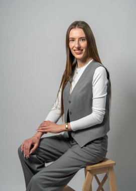 Uzun saçlı, tahta merdivende oturan genç bir kadının stüdyo portresi. Tarafsız arka planı olan minimalist bir ortam. Doğal güzellik kavramı, sadelik, modern yaşam tarzı..