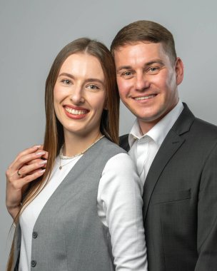 Beyaz stüdyo geçmişine karşı şık kıyafetler içinde poz veren mutlu genç çift. Gülümsüyor ve kameraya bakıyor. Kendine güvenen ve stil sahibi bir moda çekimi..