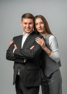 İş temalı stüdyo fotoğrafında takım elbiseli şık bir genç kadın kollarını kavuşturmuş takım elbiseli kendine güvenen bir adamın yanında duruyor. Modern şirket modası ve takım başarısı konsepti.