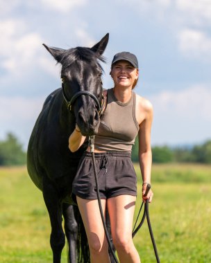 Şirin kız yeşil tarlada siyah atla vakit geçiriyor. Doğanın arka planına karşı sahne, insan ve hayvanın uyumunu, atları sevmeyi sembolize eder. Kırsal yaşam tarzı. Yaz güneşli bir gün.