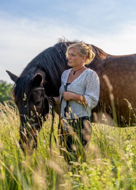 Geniş alanda genç bir kadın ve atı arasında sakin bir an. Güven ifadesi, arkadaşlık ve insan hayvan ilişkilerinin güzelliği..