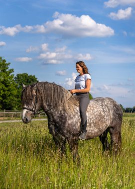 Yeşil çim tarlasında çıplak oturan bir kız. Doğal ışık, sakin kırsal atmosfer, insan ve hayvan arasındaki özgürlüğü, güveni ve uyumu simgeliyor..
