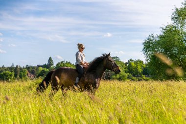 Genç bir kadının otlak arazide eyersiz dört nala koşuşunun dinamik sahnesi. Peyzaj doğa ve evcilleştirilmemiş ruhla olan bağını ifade eder.