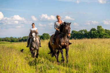 Parlak bir yaz gününde, iki kadın at sırtında geniş yeşil bir tarlada ata biniyor. Atlı maceranın ruhunu, açık havada yaşamayı ve kırsal hayatın huzurlu ritmini yakalar..