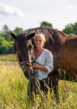Güzel bir binici yeşil alanda kahverengi atını nazikçe okşar, şefkat ve dostluk anını paylaşır. İnsanlar ve atlar arasındaki uyumu, özeni ve özel bağı sembolize eder..