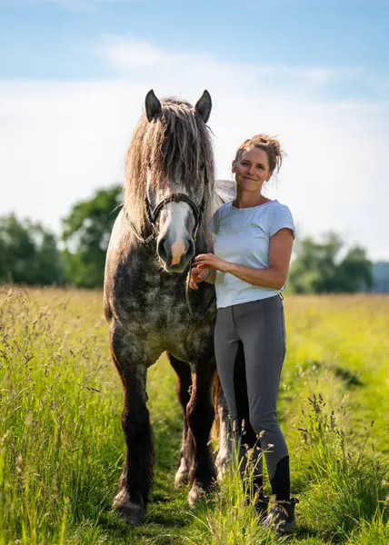 Değer veren genç binicinin sakin toprak yolda zarif gri atını kucakladığı huzurlu kırsal an. Sıcak, duygusal sahne güven, şefkat ve doğayla uyum dolu..