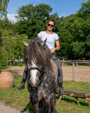 Kırsal toprak yol boyunca, açık tarım arazileriyle çevrili Dapple Gri Atı 'nda gezmekten hoşlanan bir kadın. Ülke yaşamının ve açık hava binicilik faaliyetlerinin barışçıl tasviri.