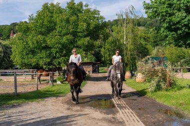 İki neşeli arkadaş kırsal alanda ata binen kadın kahkaha ve eğlenceyi paylaşıyor. Canlı bir açık hava anı dostluğu, özgürlüğü ve kır hayatının güzelliğini yakalıyor..