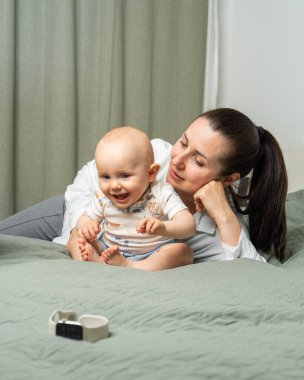 Gülümseyen anne yatakta dinlenirken meraklı oğlu kol saatine doğru sürünüyor. Erken çocukluk keşifleri, ebeveynlik ve aile bağlarını ön plana çıkaran samimi ve sıcak bir an..