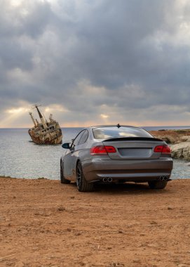 Kıbrıs 'ın kayalık kıyı şeridinde altın gün batımında, deniz enkazını dramatik bir şekilde gören modern bir araba. Mükemmel seyahat, yaşam tarzı veya otomotiv konsepti.