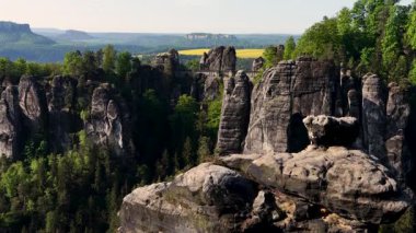 Almanya 'daki Sakson İsviçre Ulusal Parkı' ndaki uçurumlardan yayılan ünlü Bastai Köprüsü manzarası. Sarı kolza tohumu tarlası uzaktan görülebilir. Seyahat, Avrupa eğlenceleri