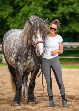 Gülümseyen kadın çiftçi kırsal alanda dapple gri atıyla bağ kuruyor. Doğal ortam hayvan bakımını, kırsal yaşamı, insan hayvan bağlantısını sembolize eder..
