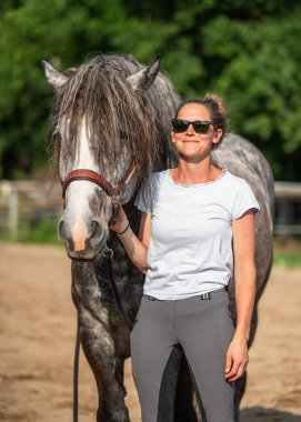Neşeli kadın çiftçi, kır çiftliğinde gri atıyla vakit geçiriyor. Açık kırsal kesimde güven, özen, otantik insan hayvan bağlantısını gösteren.