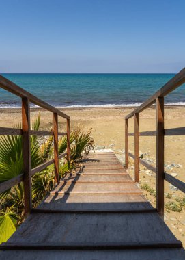 Turkuaz kıyıya doğru idilik iniş. Tahta merdiven güney Kıbrıs 'ta sakin bir sahile çıkıyor. Yumuşak deniz esintisi ve berrak suların mükemmel bir dinginlik yarattığı yer..