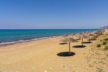 Güney Kıbrıs 'taki derin mavi denize bakan boş kumlu bir plajda saman güneş şemsiyeleri. Bir sürü kopya alanı olan minimalist yaz sahnesi, seyahat, tatil veya rahatlama kavramları için ideal.