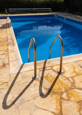 Paslanmaz çelik merdiven temiz mavi suyla yüzme havuzuna iniyor. Tatil, seyahat, boş zaman ve sağlık konuları için ideal.