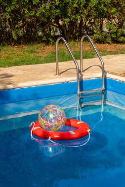 Mavi yüzme havuzunda yüzen kırmızı can simidinin içine yerleştirilmiş renkli şişme top. Çocuk güvenliğinin ve neşeli yaz anlarının sembolü. Aile, seyahat ve refah için harika..
