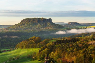 Almanya 'nın Sakson İsviçre Ulusal Parkı' ndaki Lilienstein Dağı ve Koenigstein Kalesi 'nin kayalık bakış açısından nefes kesici bir manzara. Yürüyüşçüler ve gezginler arasında popüler olan ikonik manzara.