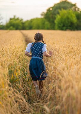Geleneksel Alman topraklarında altın buğday tarlasında koşan kız öğrenci, dikiz aynası. Örgülü saç, kırsal yaşam tarzı, çocukluk, gelenek, açık hava özgürlüğü kavramı.