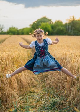 Neşeli genç kız altın buğday tarlasında yükseğe atlıyor, gülümsüyor ve dışarıda oynuyor. Çocukluk eğlencesi, özgürlük, enerji, kırsal mutluluk kavramı.