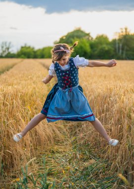 Geleneksel Alman topraklarında altın buğday tarlasına atlayan neşeli kız. Açık hava eğlencesi, çocukluk eğlencesi, kültür mirası ve kırsal özgürlük..