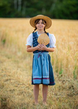 Geleneksel Bavyera dirseği ve buğday tarlasında duran hasır şapkalı çekici genç kız. Çocukluk masumiyeti kavramı, halk kültürü, kırsal yaz hayatı..