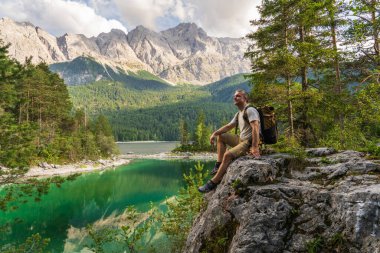 Almanya, Zugspitze yakınlarındaki Eibsee Gölü ve Bavyera Alpleri 'nin muhteşem manzarasına hayran kalan bir adam oturuyor. Doğada huzurlu bir an, seyahat, yürüyüş, macera temaları için mükemmel..