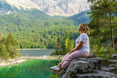 Dişi yürüyüşçü, Eibsee Gölü 'nün ve Almanya' nın Zugspitze yakınlarındaki dağların nefes kesici manzarasının keyfini çıkarıyor. Alplerde sakin bir açık hava anı.