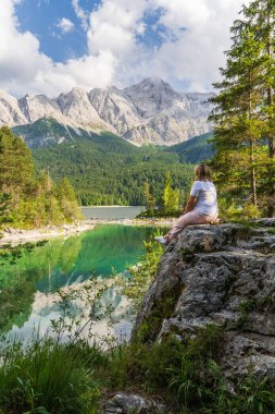 Eibsee Gölü ve Almanya 'daki Bavyera Alpleri' ne bakan kayada oturan kadın. Huzurlu alp manzarası, yürüyüş, doğa keşfi, seyahat ilhamı için ideal..