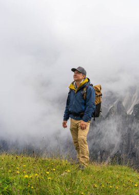 Yağmurlu havalarda Dolomitlerin içinde sırt çantalı mutlu bir adam var. Bulut kaplı dağlar. Kötü havaya rağmen seyahat ve macera kavramı.