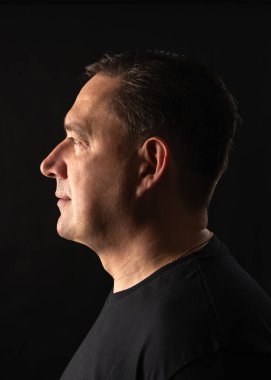 Geçmişi karanlık olan bir adamın yan profili. Ciddi, karamsar bir ses tonuyla minimalist stüdyo portresi, yüz hatlarına güçlü bir görsel odaklanma.