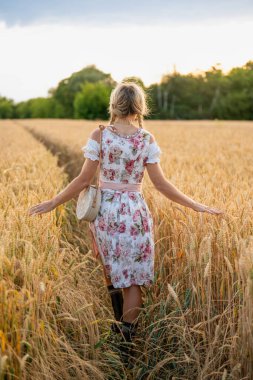 Geleneksel Bavyera dirseklerinde örülmüş saçları olan genç bir kadının tarladaki buğdaya nazikçe dokunuşu. Kırsal, kültürel, barışçıl atmosfer.