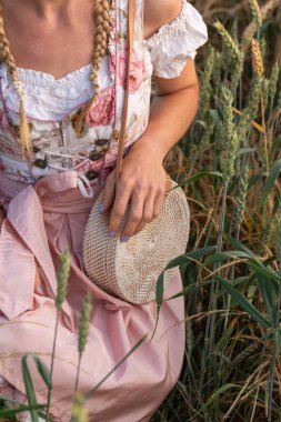 Geleneksel Bavyera elbisesi giymiş buğday tarlasında örülmüş bir kadın görüntüsü. Halk kostümleri, kırsal yaşam tarzı, güneşli bir yaz gününde kültürel atmosfer..