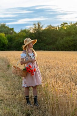 Folk Bavyera kıyafetleri ve altın buğday tarlasında sepeti tutan hasır şapkalı çekici bir genç kadın. Geleneğin barışçıl karışımı, kırsal güzellik, mevsimsel sıcaklık.