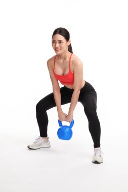 Çaydanlık çanlarıyla egzersiz yapan atletik bir kadın, beyaz arka planda spor kıyafetleriyle spor yapmaya hazır genç Asyalı güzel bir kadın.